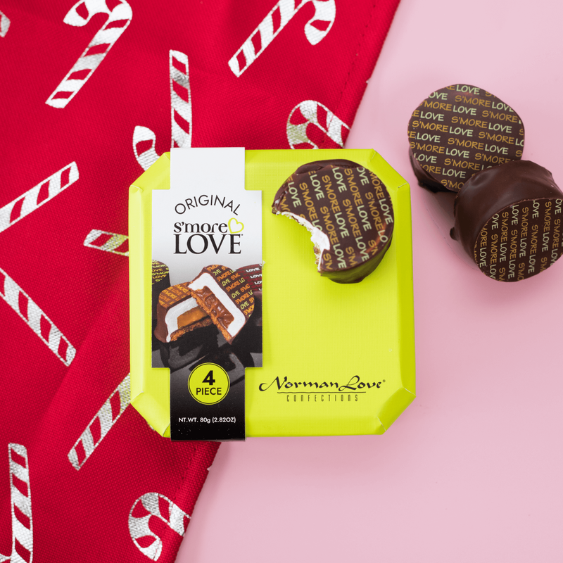Three S'mores Love candies displayed on a pink and red candy cane background. One candy has a bite taken out of it to show the gooey marshmallow inside.